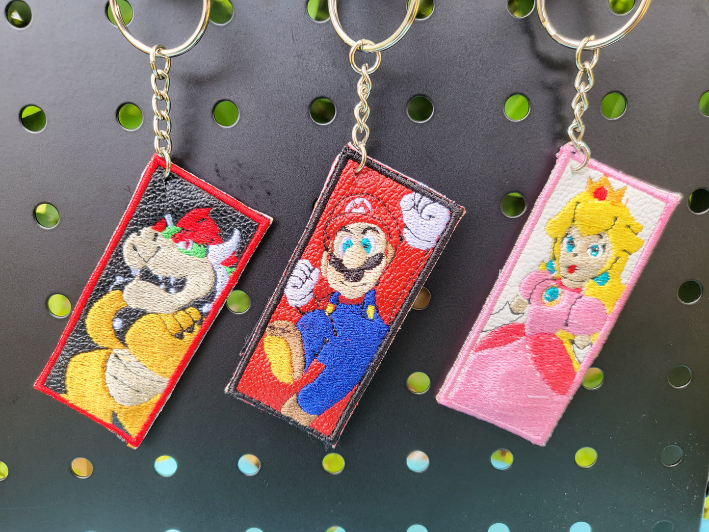 Three magnetic keychains featuring animated characters from the Mario series, displayed on a metal grid background.